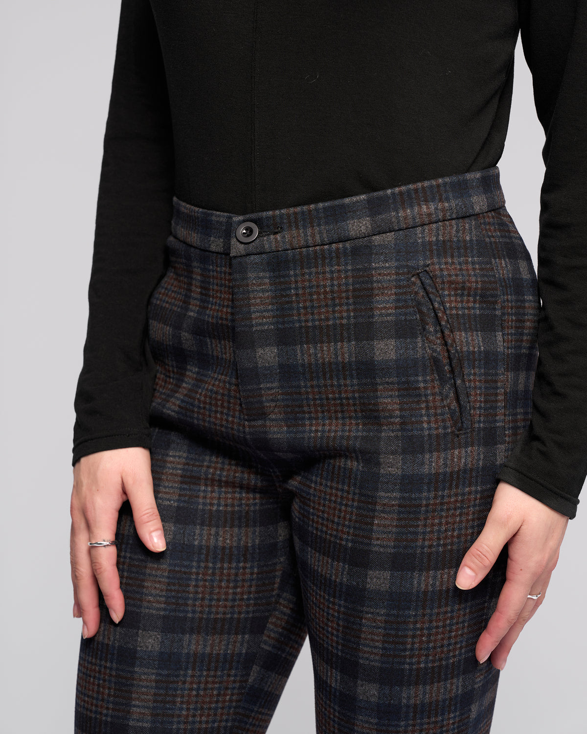 A person is wearing a black long-sleeve top and Vassalli Style Pant - Nomad in gray with brown stripes, standing with arms relaxed, visible from mid-torso to mid-thigh.