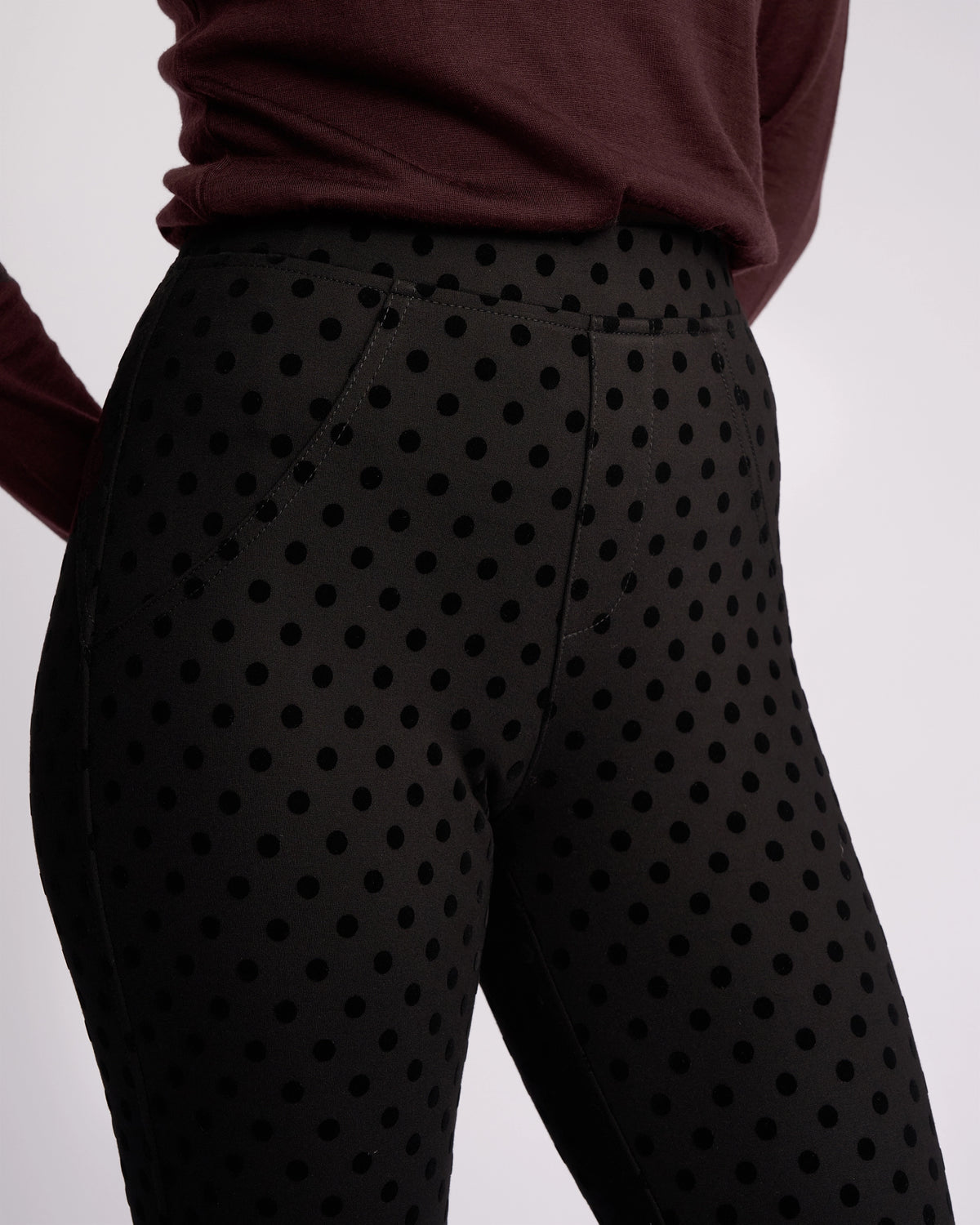 A person wearing Vassalli’s View Pant - Black, ankle-grazer high-waisted pants with large black polka dots, paired with a long-sleeved maroon top, is photographed from the waist down against a plain background.