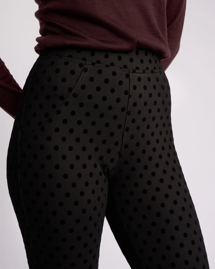 A person wearing Vassalli’s View Pant - Black, ankle-grazer high-waisted pants with large black polka dots, paired with a long-sleeved maroon top, is photographed from the waist down against a plain background.