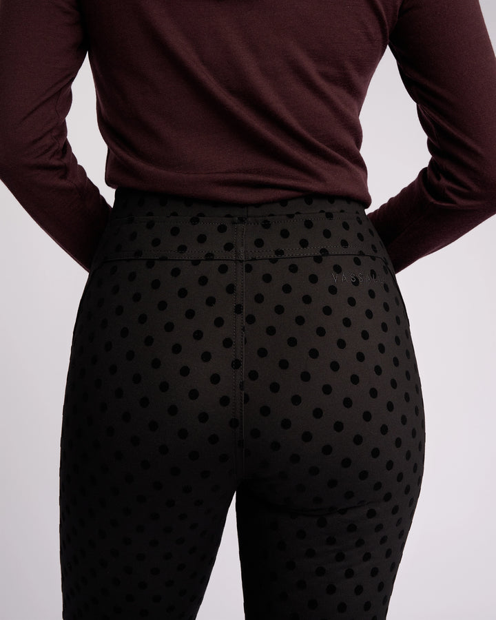 A person is shown from the back against a plain light background, wearing Vassalli’s View Pant - Black, a high-waisted skinny-leg pant in ponti fabric with black velvet polka dots, paired with a long-sleeved maroon top.