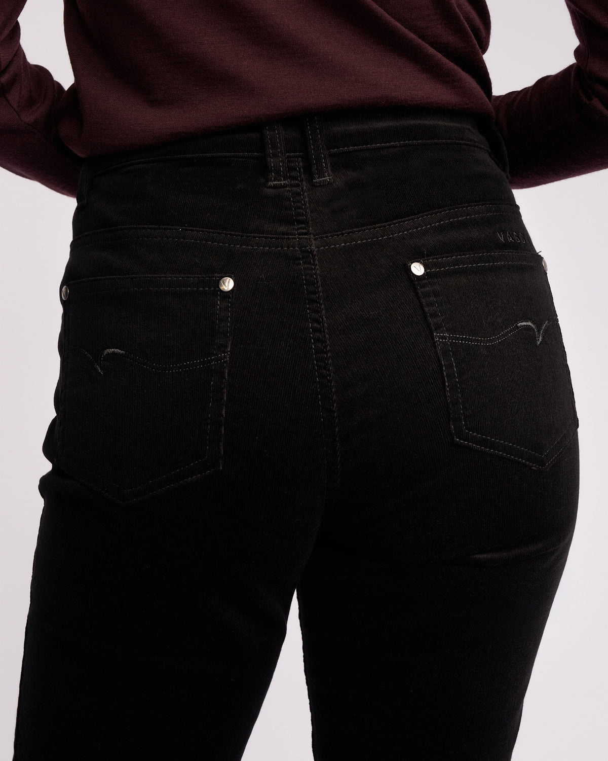 A person wearing Vassalli's Arch Cord Pant - Black, paired with a long-sleeved dark burgundy top, shown from the waist down with their back to the camera—a chic winter wardrobe staple.