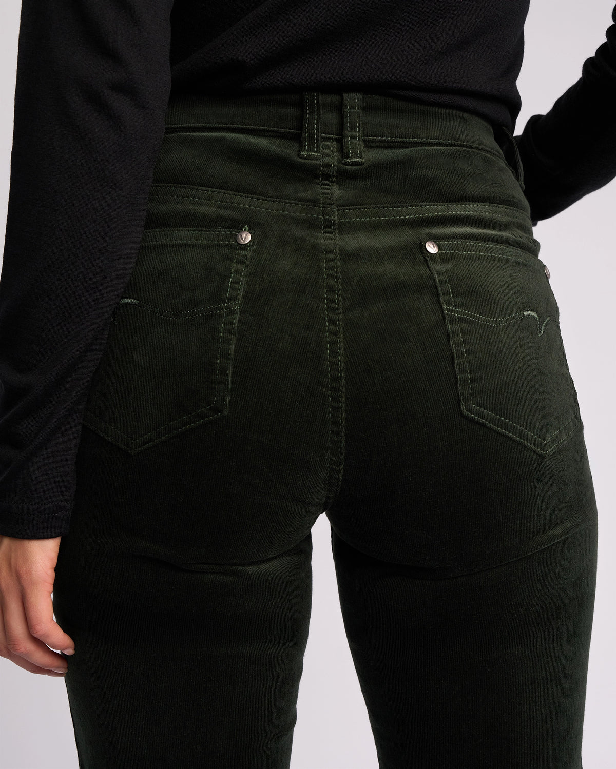 A person is shown from the back wearing Vassalli’s Arch Cord Pant in Forest and a long-sleeve black shirt, highlighting the pocket details—an essential addition to any winter wardrobe.
