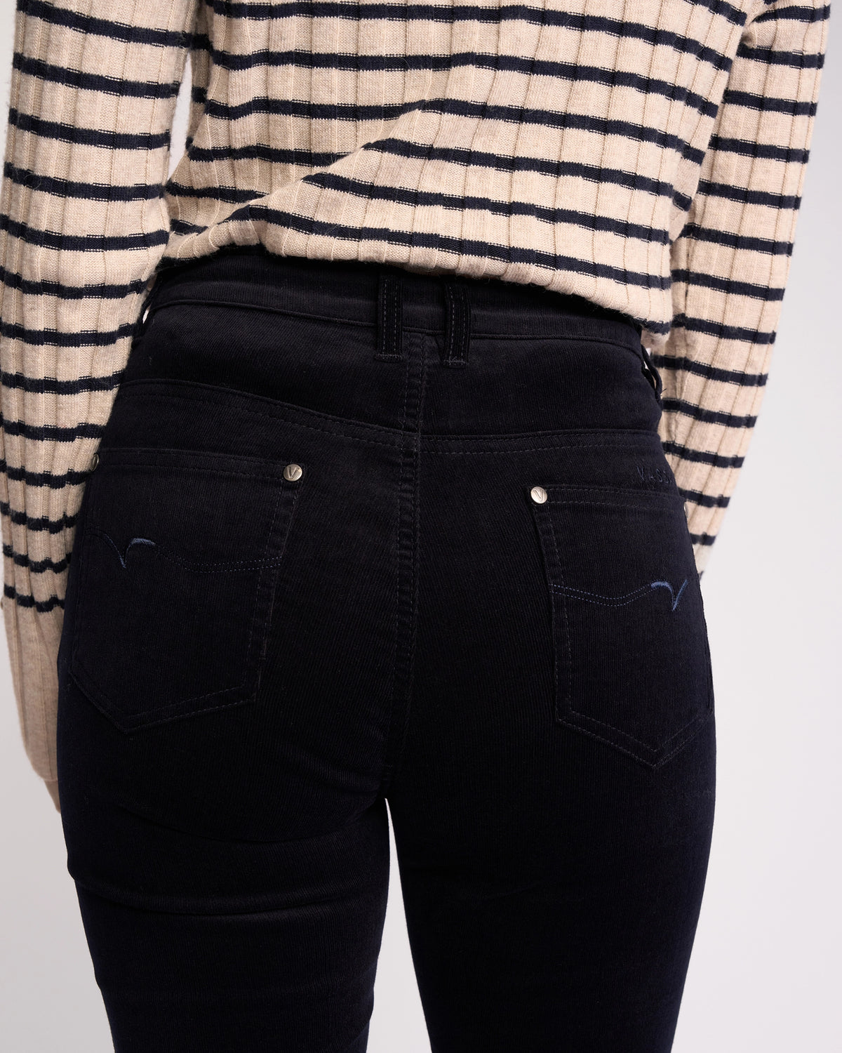 A person seen from the back wears a cream and black striped sweater with Vassalli’s Arch Cord Pant in Midnight—an effortless choice for any winter wardrobe.