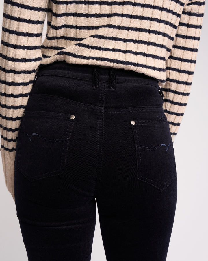 A person seen from the back wears a cream and black striped sweater with Vassalli’s Arch Cord Pant in Midnight—an effortless choice for any winter wardrobe.