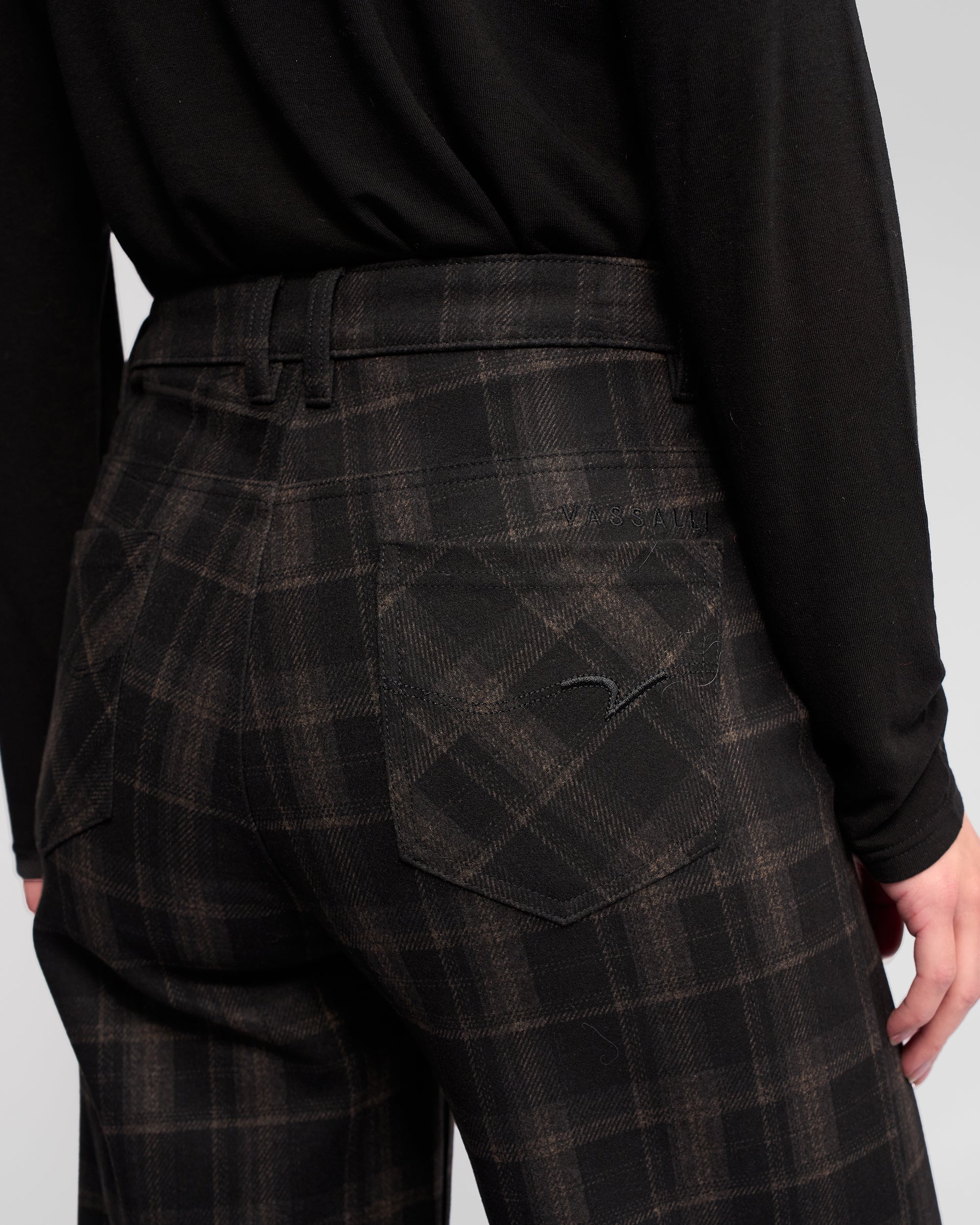 Model wearing Vassalli’s Empire Pant - Checkmate in black and brown check, seen from the back with a black long-sleeve shirt tucked in—a stylish winter look.