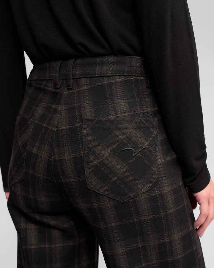 Model wearing Vassalli’s Empire Pant - Checkmate in black and brown check, seen from the back with a black long-sleeve shirt tucked in—a stylish winter look.