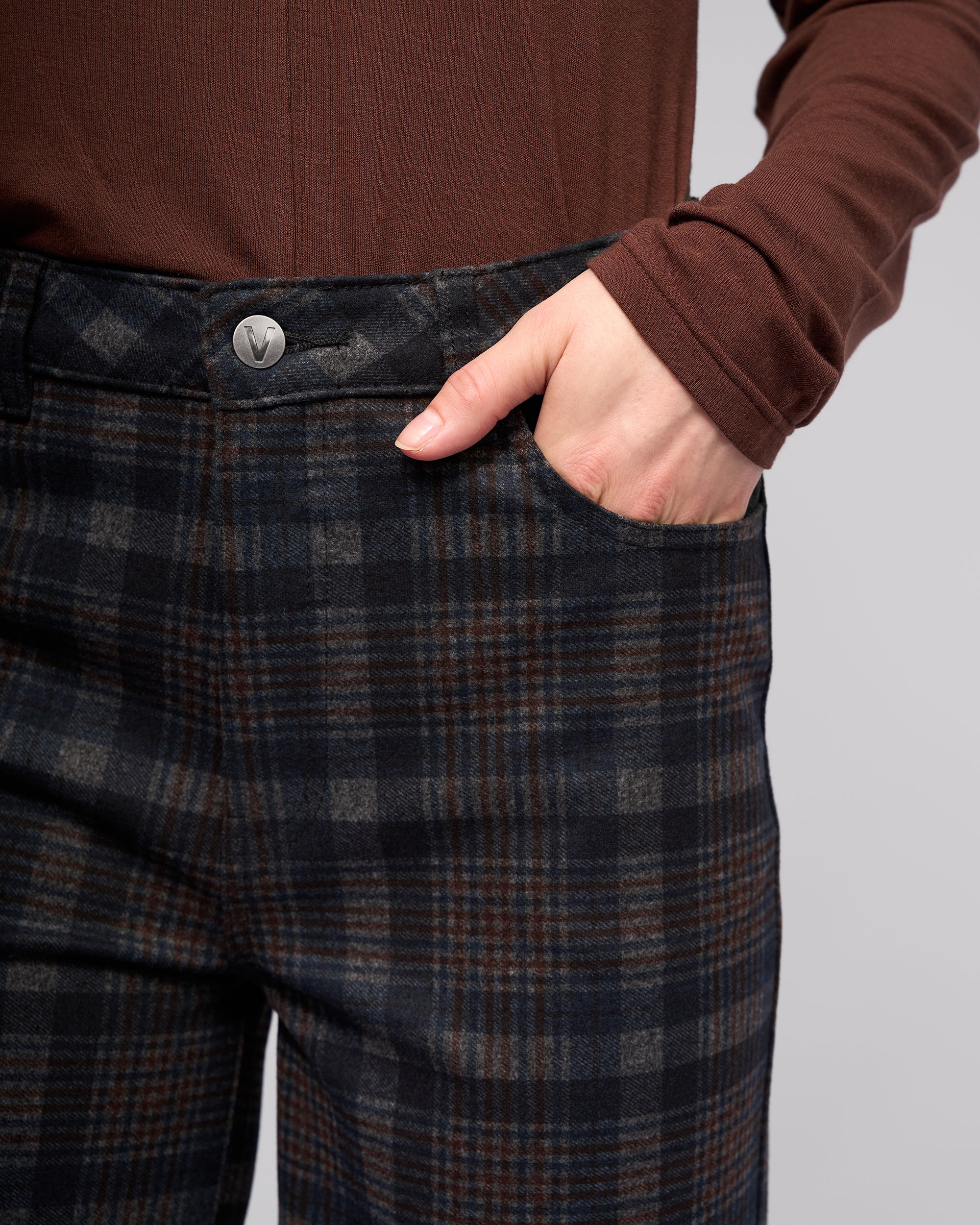 A person wears a brown long-sleeve shirt and Vassalli's Empire Pant - Nomad, one hand in the pocket, shown waist down against a plain background—perfect for winter.