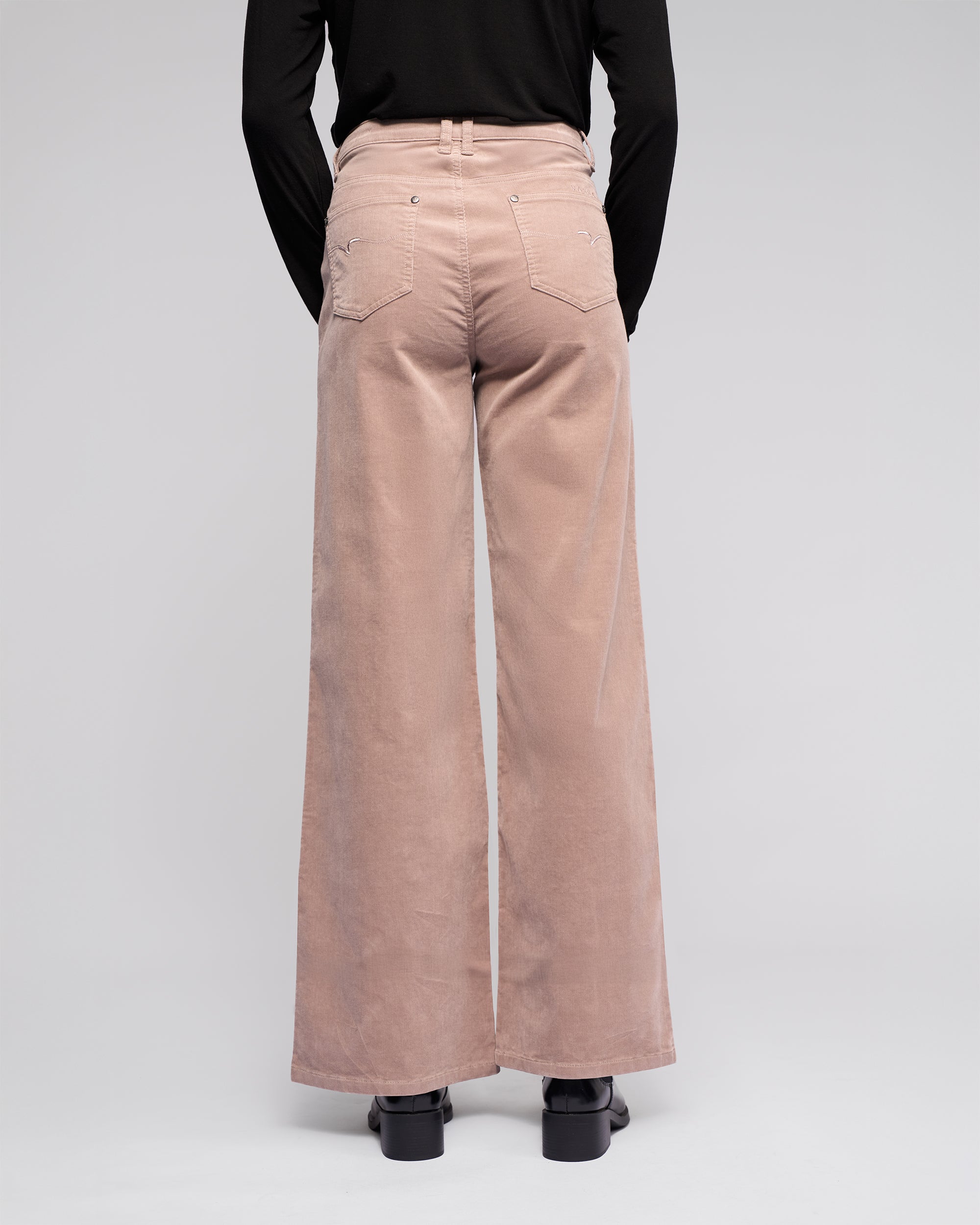 A person models the Vassalli Empire Cord Pant in Twig, a high-waisted, wide-leg corduroy style, paired with a black long-sleeve top and shown from the back against a plain light background.