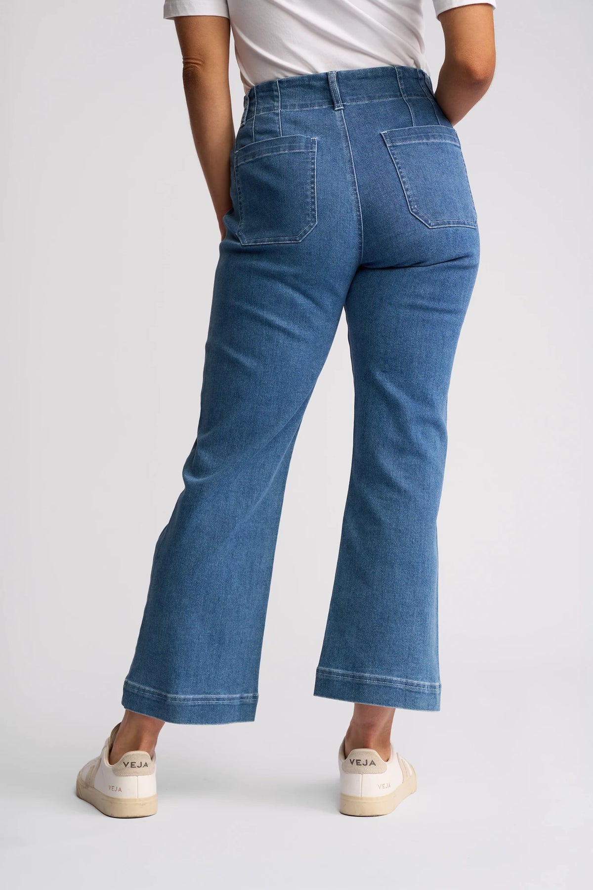A person wearing Vassalli Daily Jean - Blue Hue Denim, styled high-waisted with a straight-leg fit, stands with their back to the camera against a plain background.
