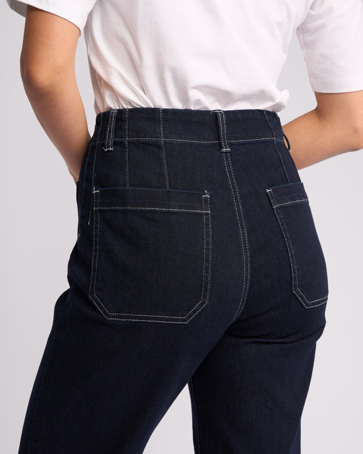 A person wearing Vassalli Daily Jean - Ink Denim, high-waisted dark blue straight leg jeans with white stitching, and a white T-shirt, shown from the waist down and viewed from behind.