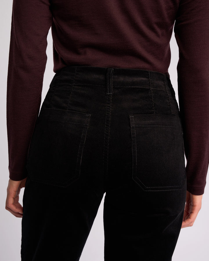 A person is shown from the back, wearing a long-sleeved maroon top and Vassalli Daily Cord Pant in black, with focus on the waist and hip area.