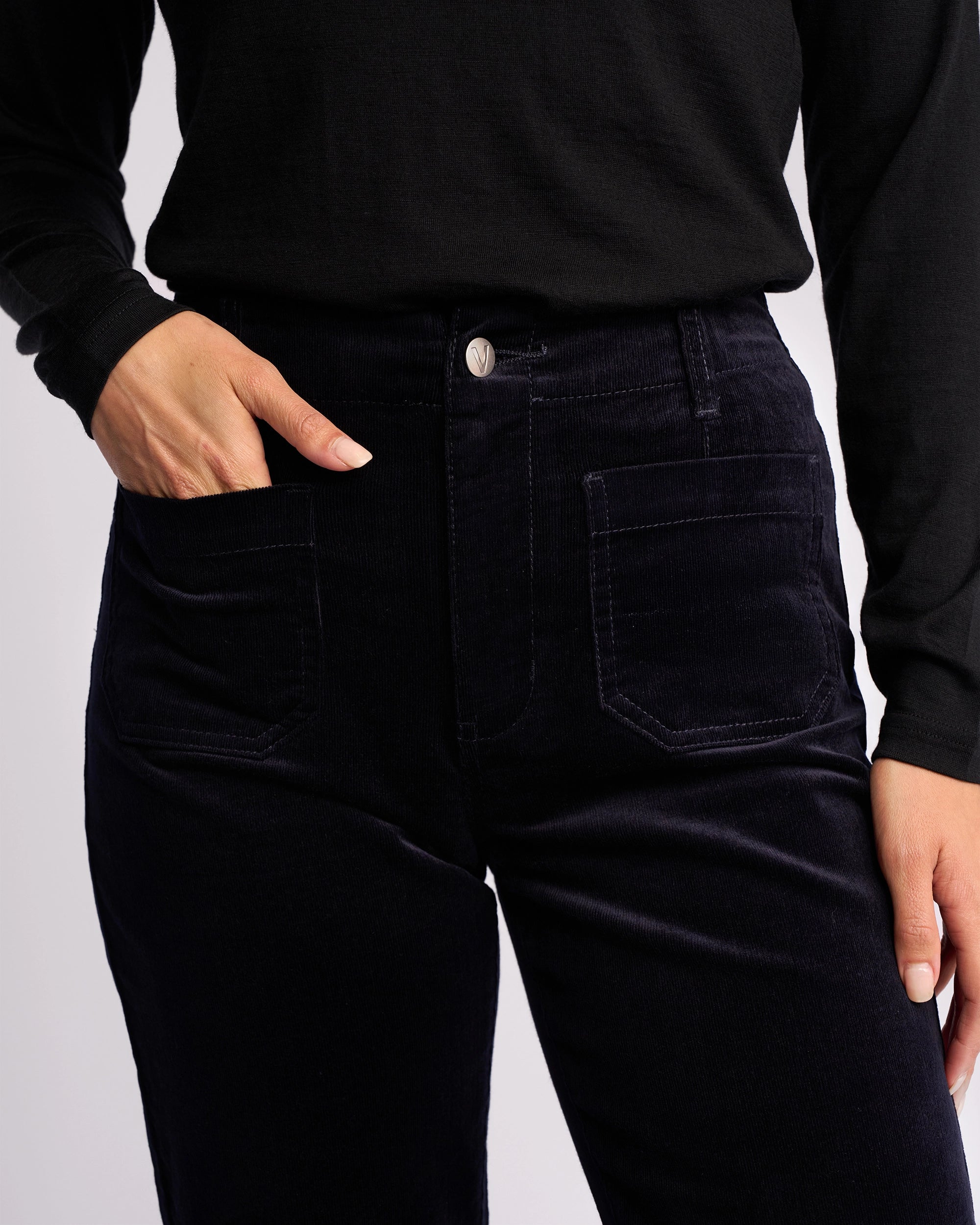 A person wears the Vassalli Daily Cord Pant - Midnight, a high-waisted, straight-leg cord pant with front pockets. Shown from shoulders to mid-thigh, one hand is in a pocket while the other rests by their side.