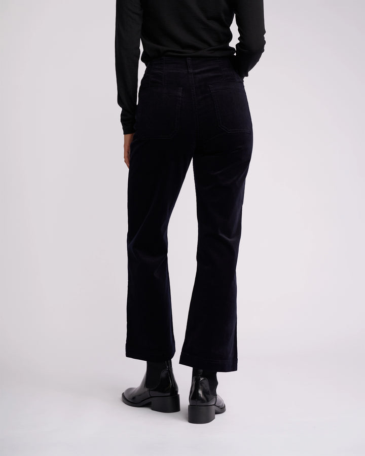 A person is shown from the back against a white background, wearing a black long-sleeve top, black ankle boots, and Vassalli’s Daily Cord Pant in Midnight—a straight-leg, high-waisted style with back pockets.