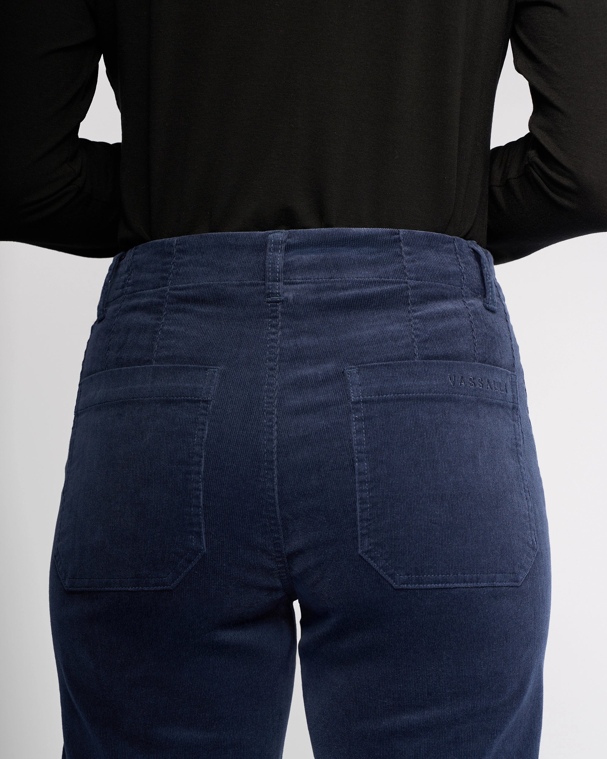 A person shown from the back wears a black long-sleeve top and Vassalli’s Daily Cord Pant in Slate, with focus on the pinwale cord waistband and high-waisted, straight-leg design with back pockets.