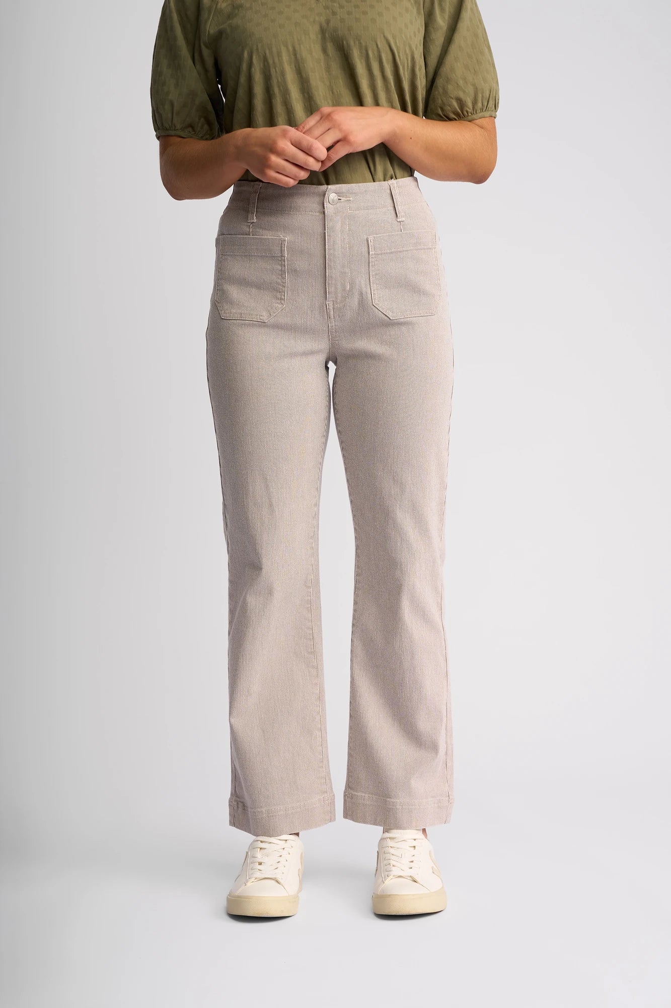 A person wearing a short-sleeve olive green top, white sneakers, and the Vassalli Daily Jean - Ecru Stripe Denim stands against a plain, light gray background.