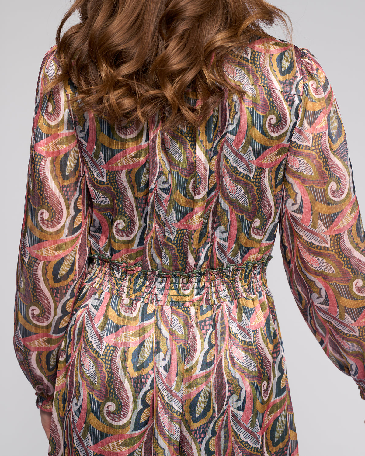 A person with wavy light brown hair is shown from behind in the Vassalli Jane Dress - Sable, a long-sleeve dress with colorful abstract swirls and a cinched waist, perfect for adding flair to any wardrobe.