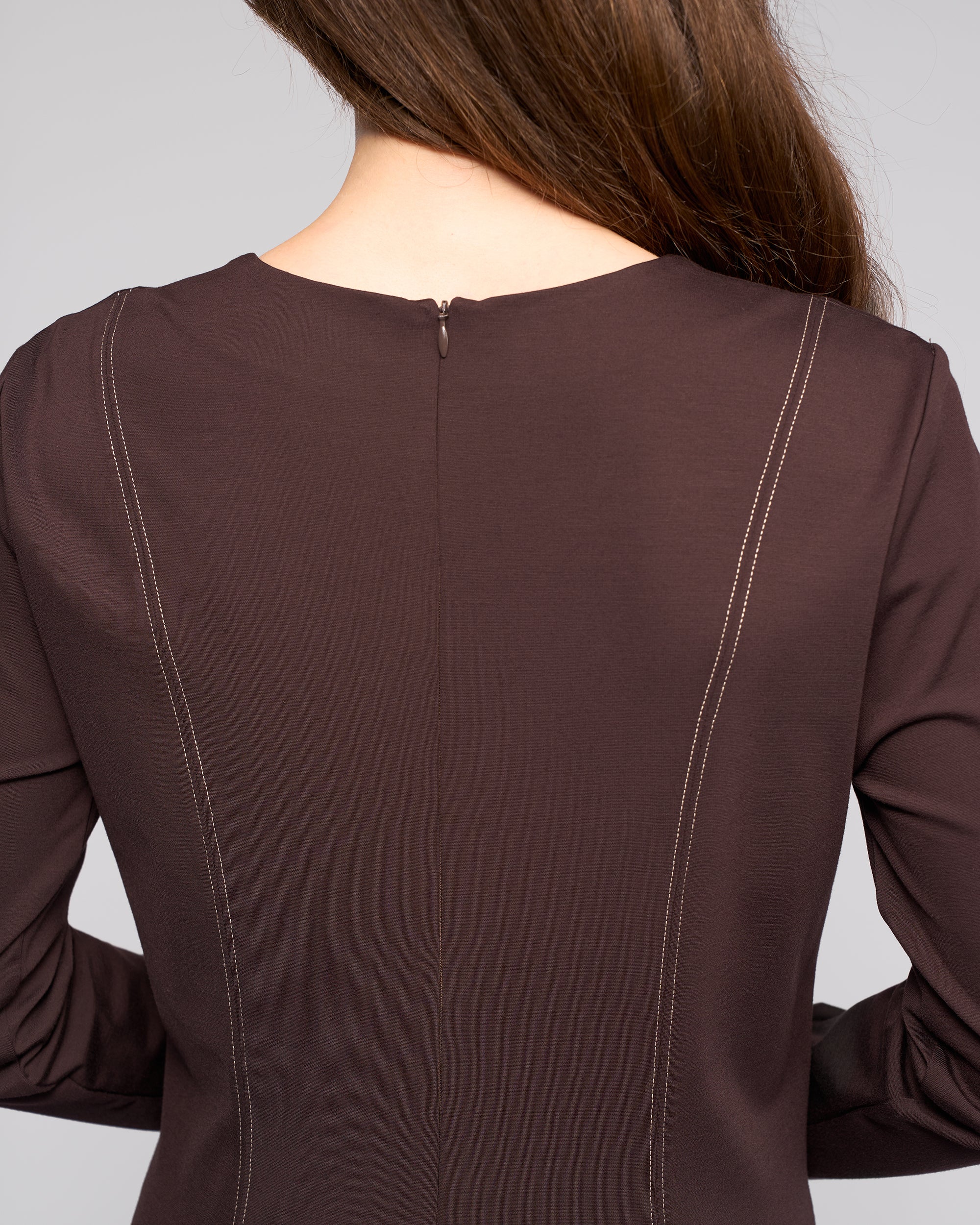 A person with long brown hair is shown from behind, wearing the Vassalli Miner Dress - Chocolate, featuring visible vertical stitching and a small zipper at the neckline for a flattering silhouette.