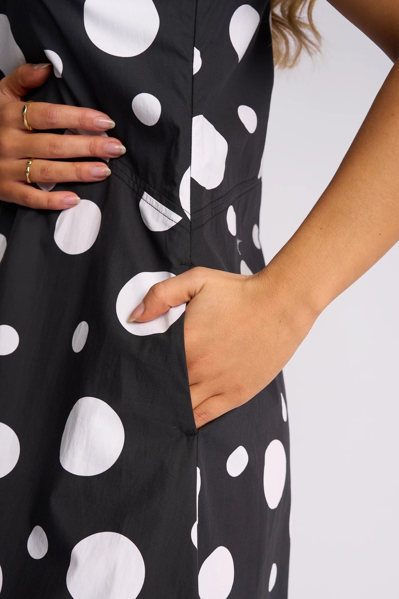 A person wearing the Vassalli Blake Dress – Spot has one hand in the pocket and the other resting on their waist, displaying gold rings.