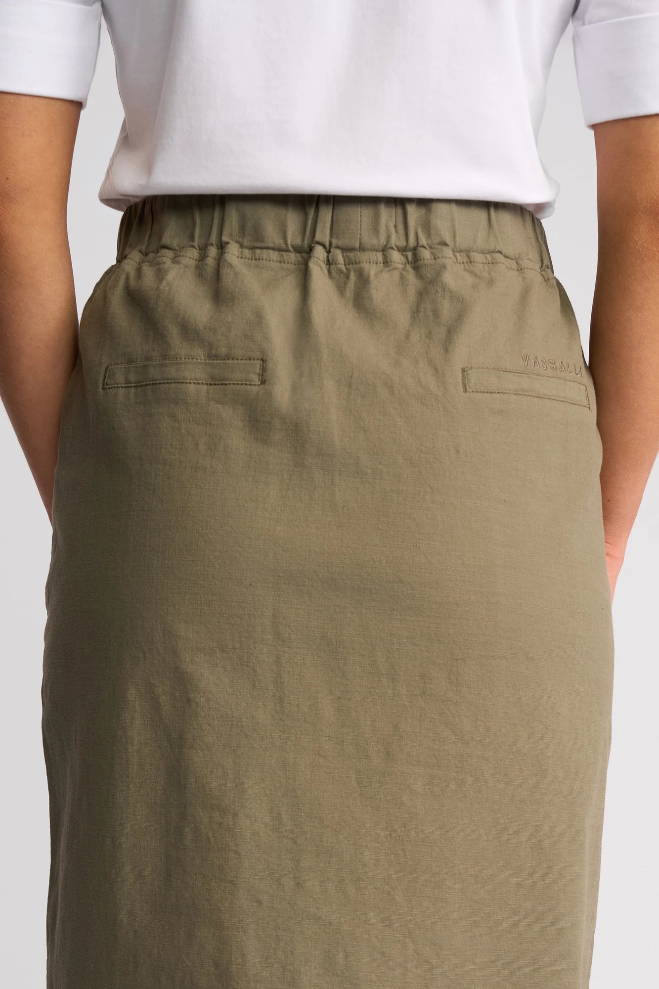 A person wearing a white shirt and an olive green Vassalli Belen Skirt - Army, shown from the waist down with hands at their sides.