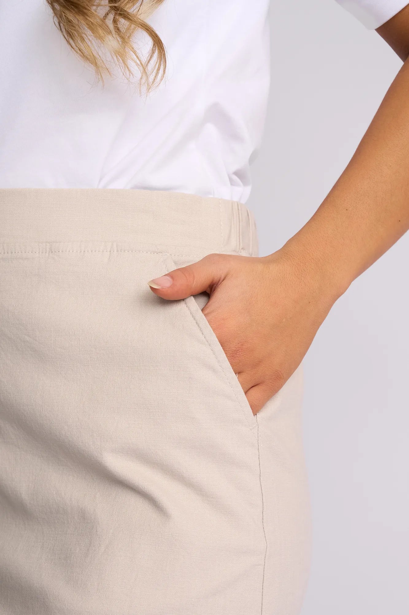 A person wearing a white shirt and the Vassalli Belen Skirt - Stone stands with one hand in the skirt pocket. Only the torso and upper legs are visible.