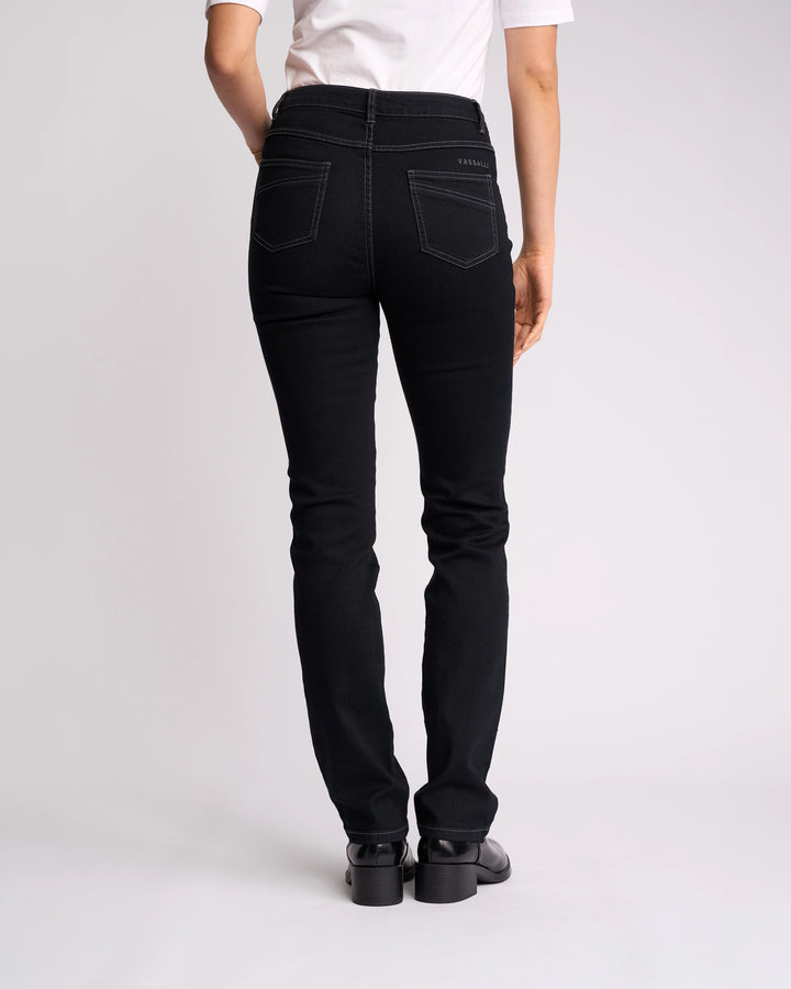 A person is standing facing away from the camera against a plain light background, wearing a white t-shirt, black shoes, and Vassalli Studio Jean - Black Denim.
