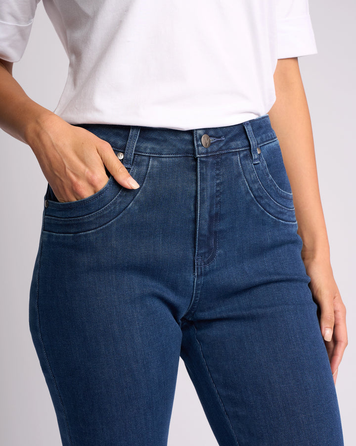 A person models the Vassalli Studio Jean - Blue Denim, pairing it with a white shirt. Shown from shoulders to thighs, they pose with one hand in a pocket and the other by their side against a plain backdrop.