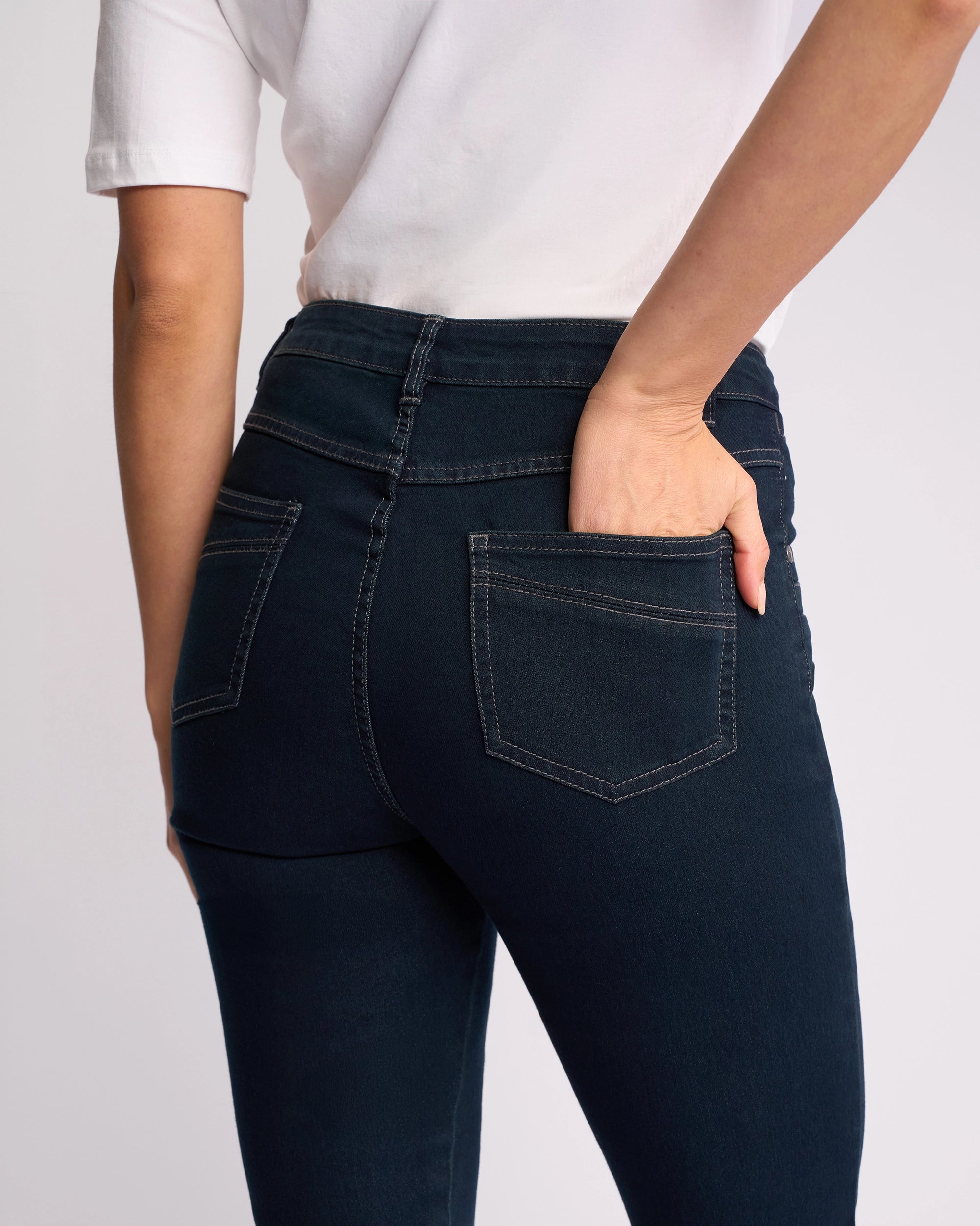 Model wearing Vassalli Studio Jean - Indigo Denim, shown from the back and waist down, with their left hand in the back pocket and paired with a white t-shirt.
