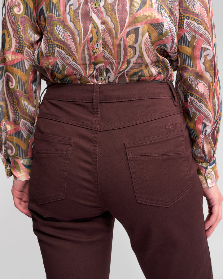 A person is shown from the back wearing Vassalli Studio Jean - Merlot, high-waisted stretch denim pants, paired with a colorful patterned long-sleeve blouse, highlighting the waist and upper legs.