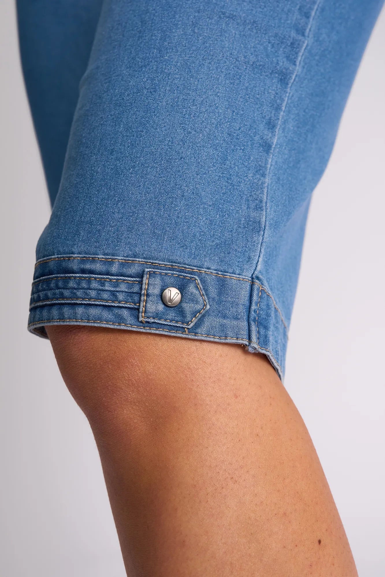 Close-up of a person’s knee wearing the Vassalli Custom Short - Light Denim, featuring a decorative metal button and stitched detailing near the hem.