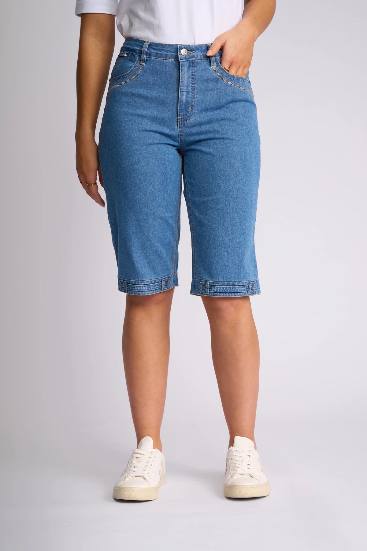 Model wearing Vassalli’s Custom Short - Light Denim, a knee-length, stretch denim short, styled with white sneakers and a white shirt against a plain light background. Only the lower half of the body is visible.