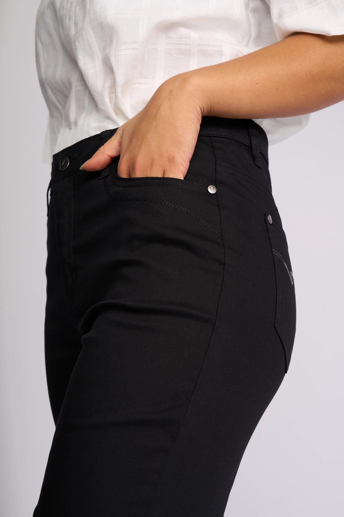 Model wearing the Vassalli Custom Lightweight Short - Black, a high-waisted black cotton-elastane short, paired with a white shirt; one hand is placed in the front pocket. Shown from mid-torso to mid-thigh against a plain background.
