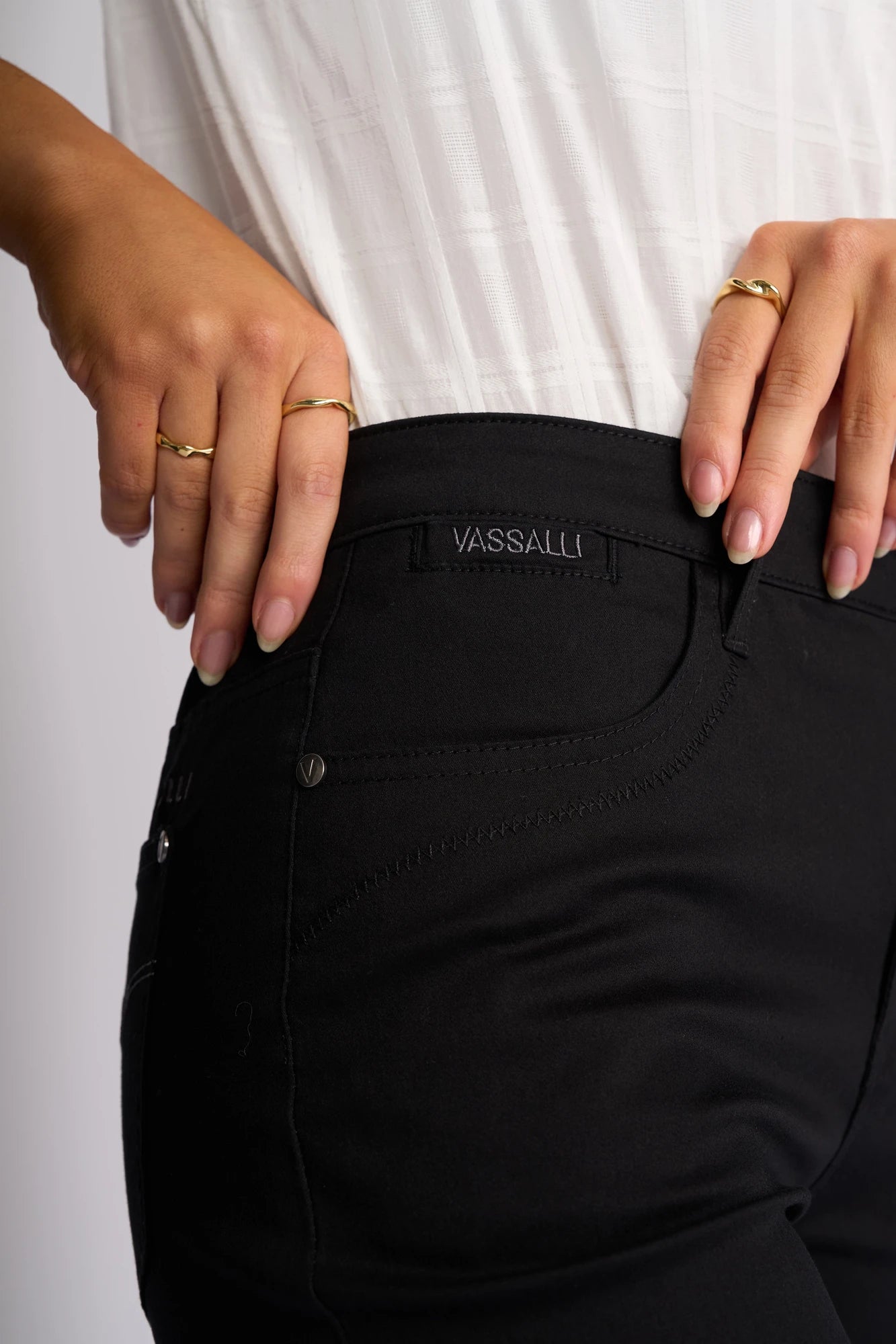 Close-up of a person wearing Vassalli Custom Lightweight Short - Black and a white textured shirt, with one hand on their hip and the other by the pocket. The person is accessorized with gold rings on both hands.