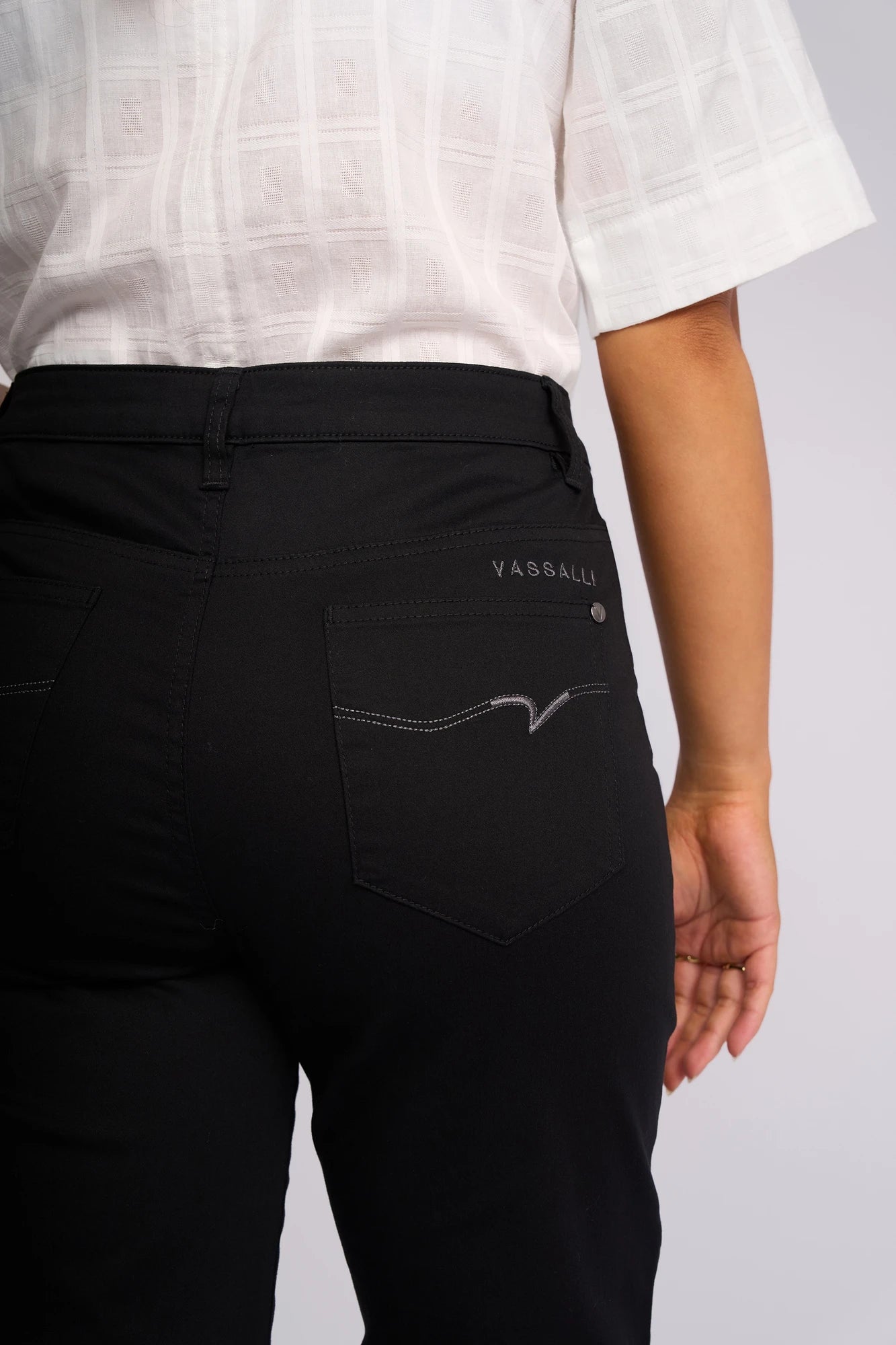 A person wearing Vassalli’s Custom Lightweight Short in black and a white short-sleeved top, shown from the back with their right arm slightly bent. The look channels the effortless style of black straight-leg shorts, perfect for casual outings.