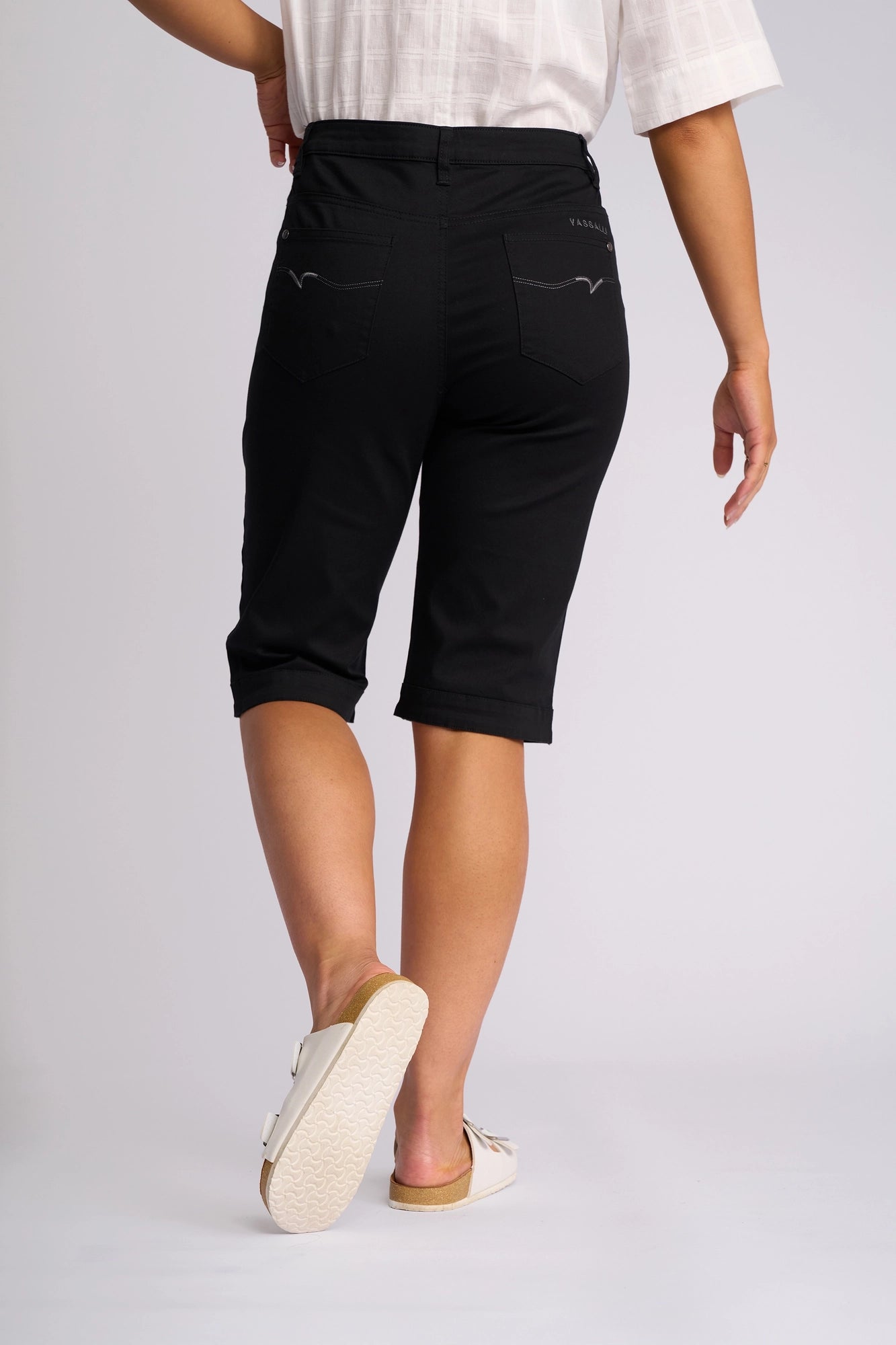 A person is wearing the Vassalli Custom Lightweight Short in black, paired with a white short-sleeve top and white slip-on shoes, standing with their back to the camera against a plain light background.