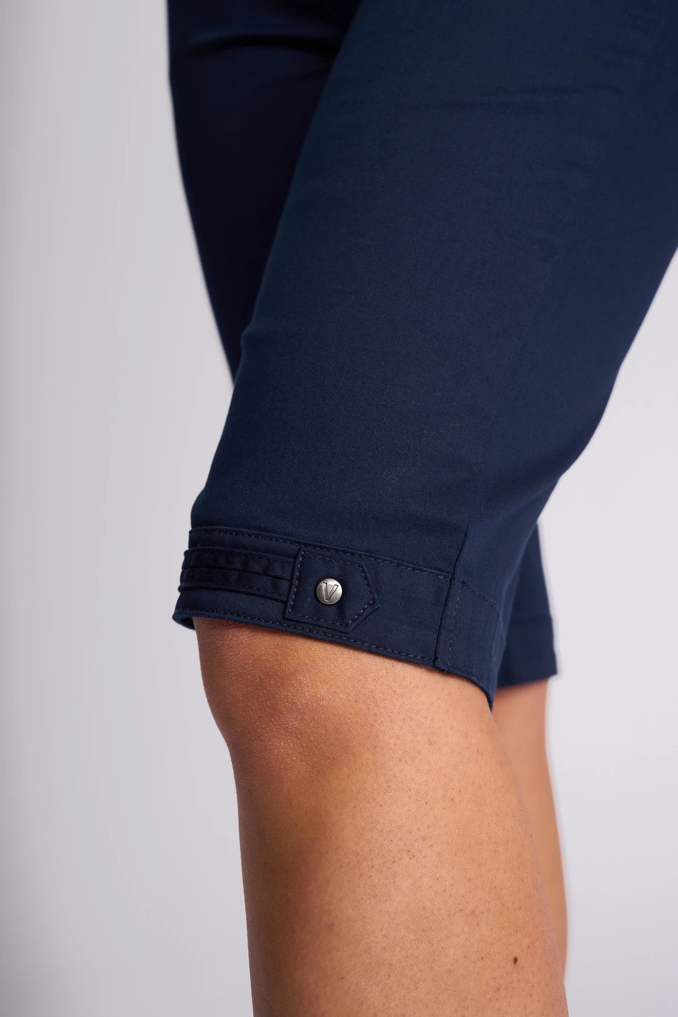 Close-up of a person’s bent knee wearing the Vassalli Custom Lightweight Short in navy, featuring cotton-elastane fabric, a decorative button, and stitched detailing near the hem.