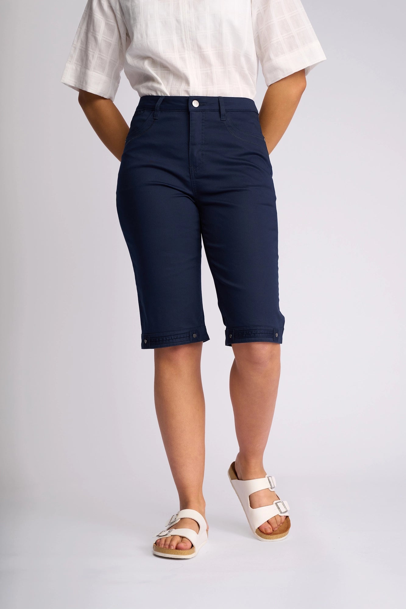 A person wearing a white short-sleeve shirt, Vassalli Custom Lightweight Short in navy, and white sandals, standing against a plain light background.