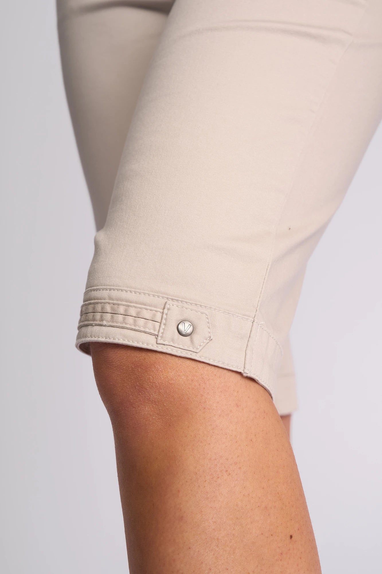 Close-up of a person wearing the Vassalli Custom Lightweight Short in Pumice—a light beige, cropped style crafted from a soft cotton-elastane blend—showing the knee area and a decorative button detail near the hem; perfect for effortless summer dressing.