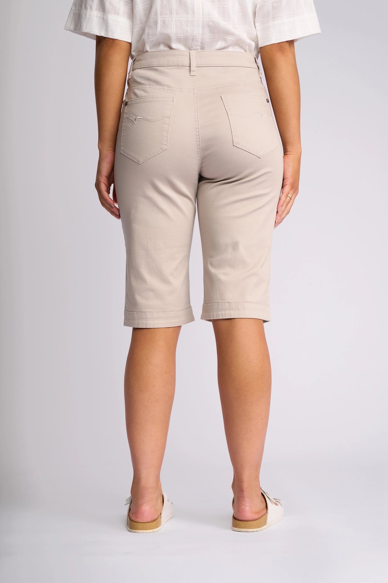 A person stands facing away from the camera, showcasing the back view of the Vassalli Custom Lightweight Short in Pumice paired with a white shirt—an ideal choice for effortless summer dressing that highlights the shorts’ pockets and relaxed style.