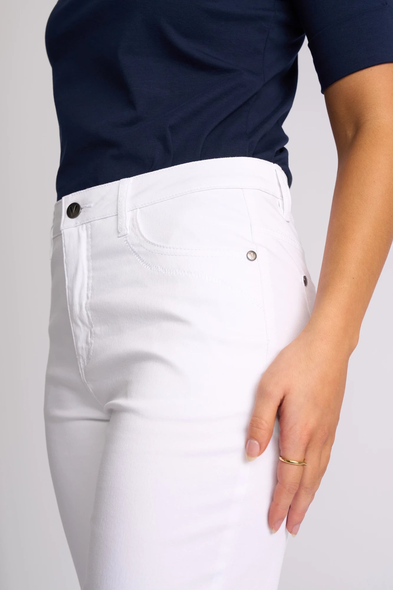 A person stands with their left hand resting by their side, wearing the Vassalli Custom Lightweight Short in White, styled with a navy blue top for effortless summer dressing. A gold ring adorns their left hand. The image is cropped from shoulders to mid-thigh.