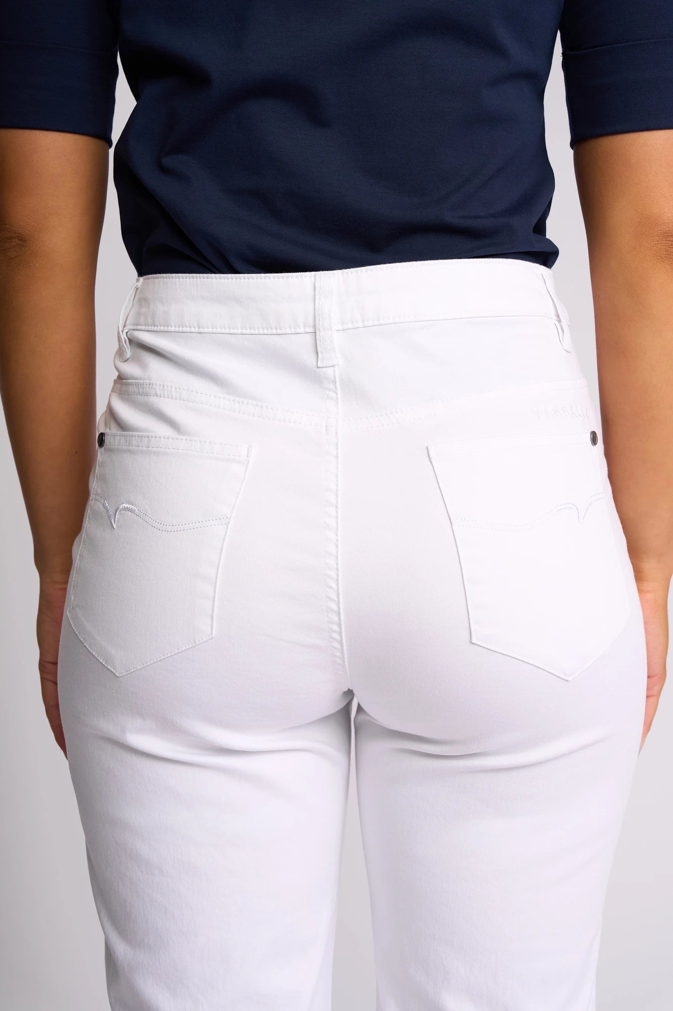 A person is shown from the back wearing a navy blue shirt and Vassalli Custom Lightweight Short in white. The summer shorts feature two back pockets and visible stitching. The background is plain and light-colored.