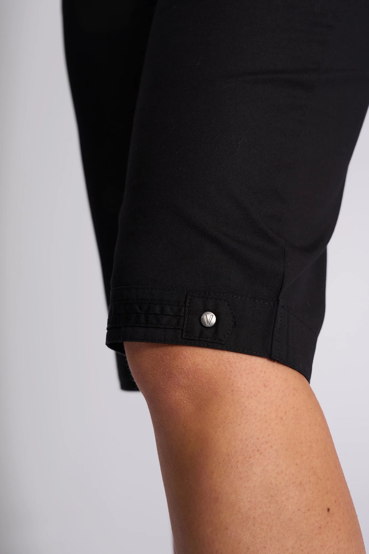 Close-up of a person’s leg wearing the Vassalli Custom Poplin Short in black, showcasing visible stitching and a small metallic button detail near the hem—a lightweight summer staple.