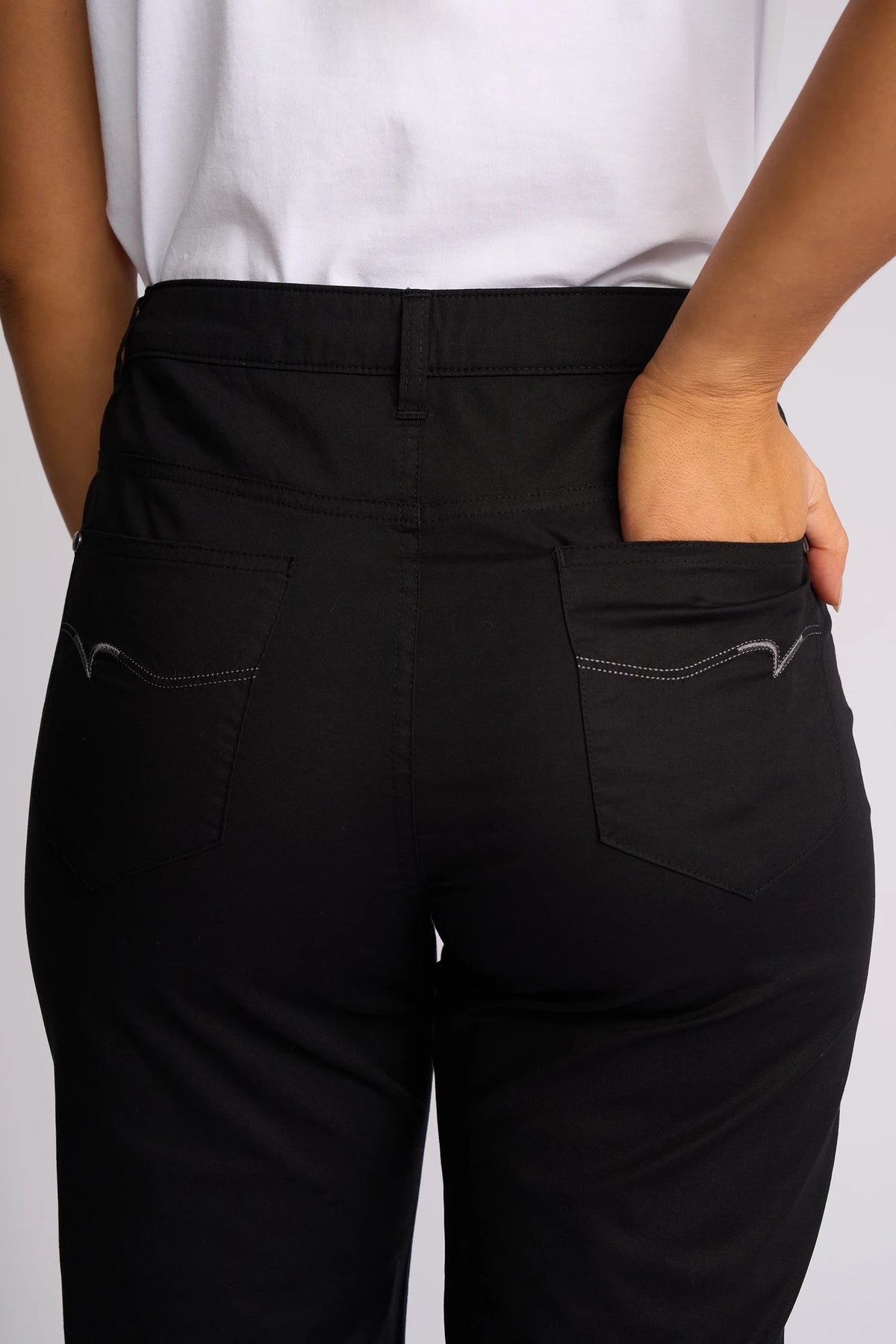A person is shown from the waist down and from behind, wearing Vassalli’s Custom Poplin Short in black with one hand in their back pocket, styled with a classic white shirt—an effortless summer staple.