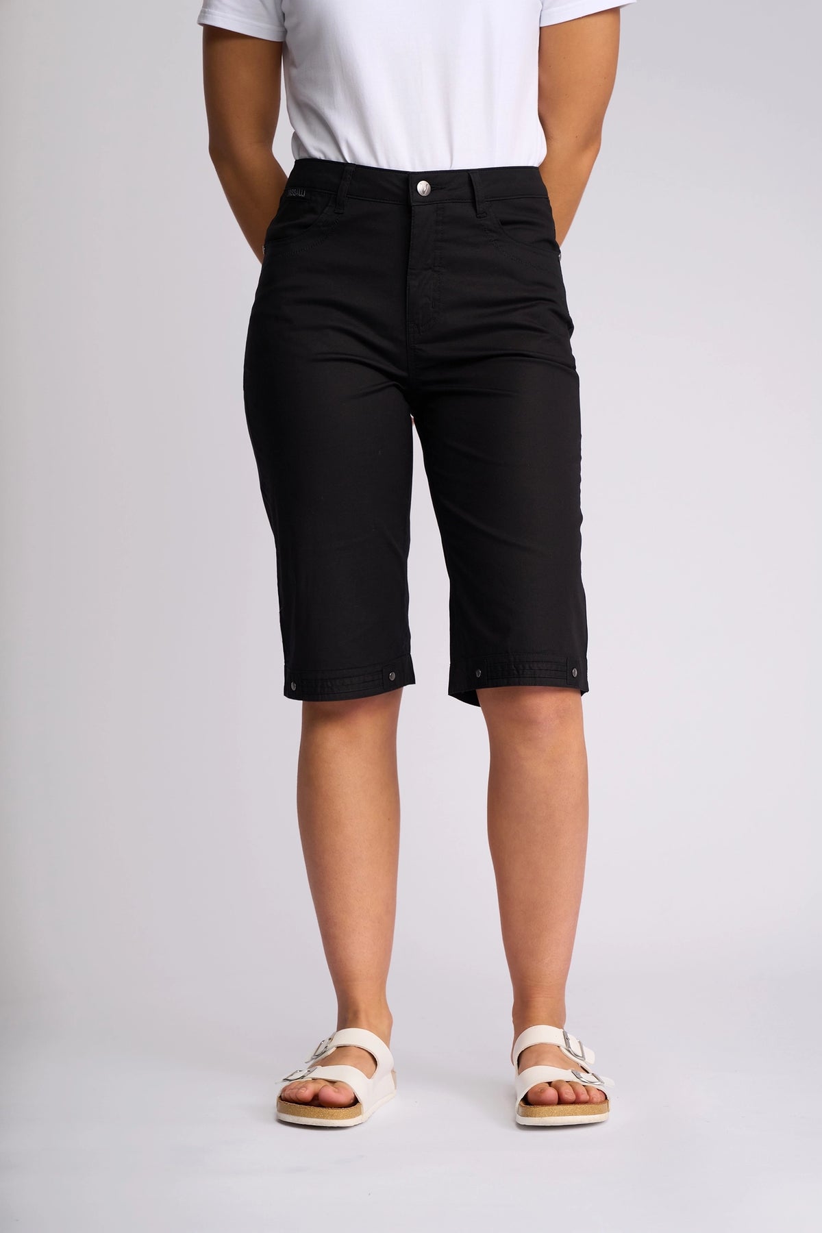 A person is shown from the shoulders down, standing against a plain background and wearing Vassalli’s Custom Poplin Short in black, paired with a white t-shirt and white sandals—creating a classic lightweight summer look.