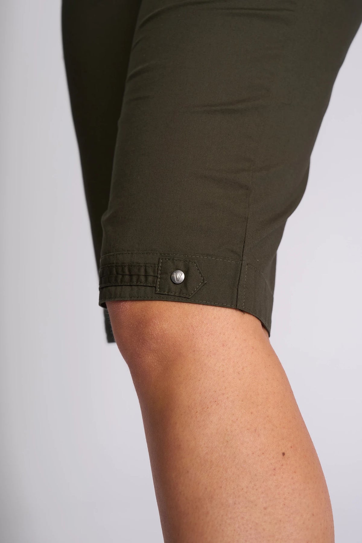 Close-up of a person’s knee wearing the Vassalli Custom Poplin Short in khaki, featuring a buttoned tab detail near the hem, set against a neutral background.