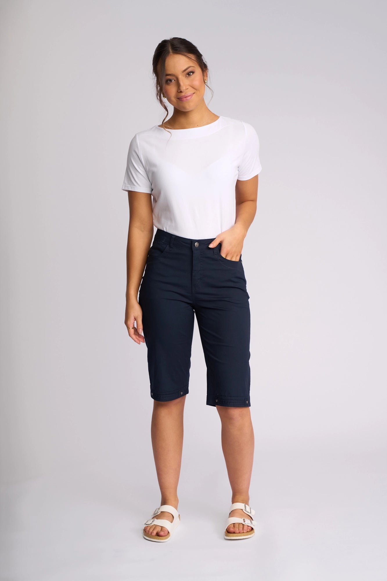A person stands against a plain background, wearing a white short-sleeve shirt, Vassalli’s Custom Poplin Short in navy, and white sandals, with one hand in their pocket and a relaxed expression—a breathable summer staple look.