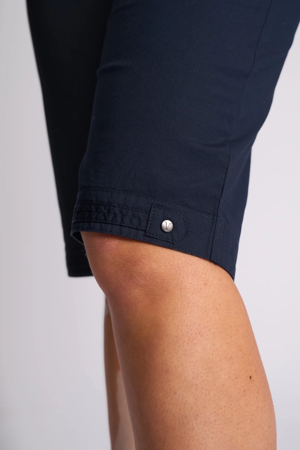 A close-up of a person wearing the Vassalli Custom Poplin Short in navy, featuring a metal button detail near the hem and a relaxed, straight-leg fit with a slightly bent knee—an ideal breathable summer staple.