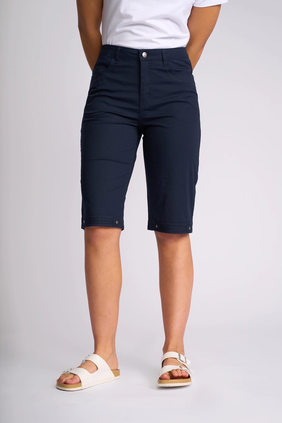 A person stands against a plain white background, cropped at the shoulders, wearing a white t-shirt, Vassalli Custom Poplin Short in Navy, and white sandals.