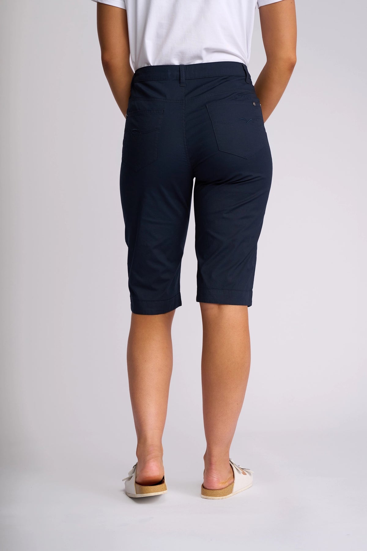 A person wearing a white t-shirt, Vassalli Custom Poplin Short in navy, and white slip-on shoes stands with their back to the camera against a plain background.