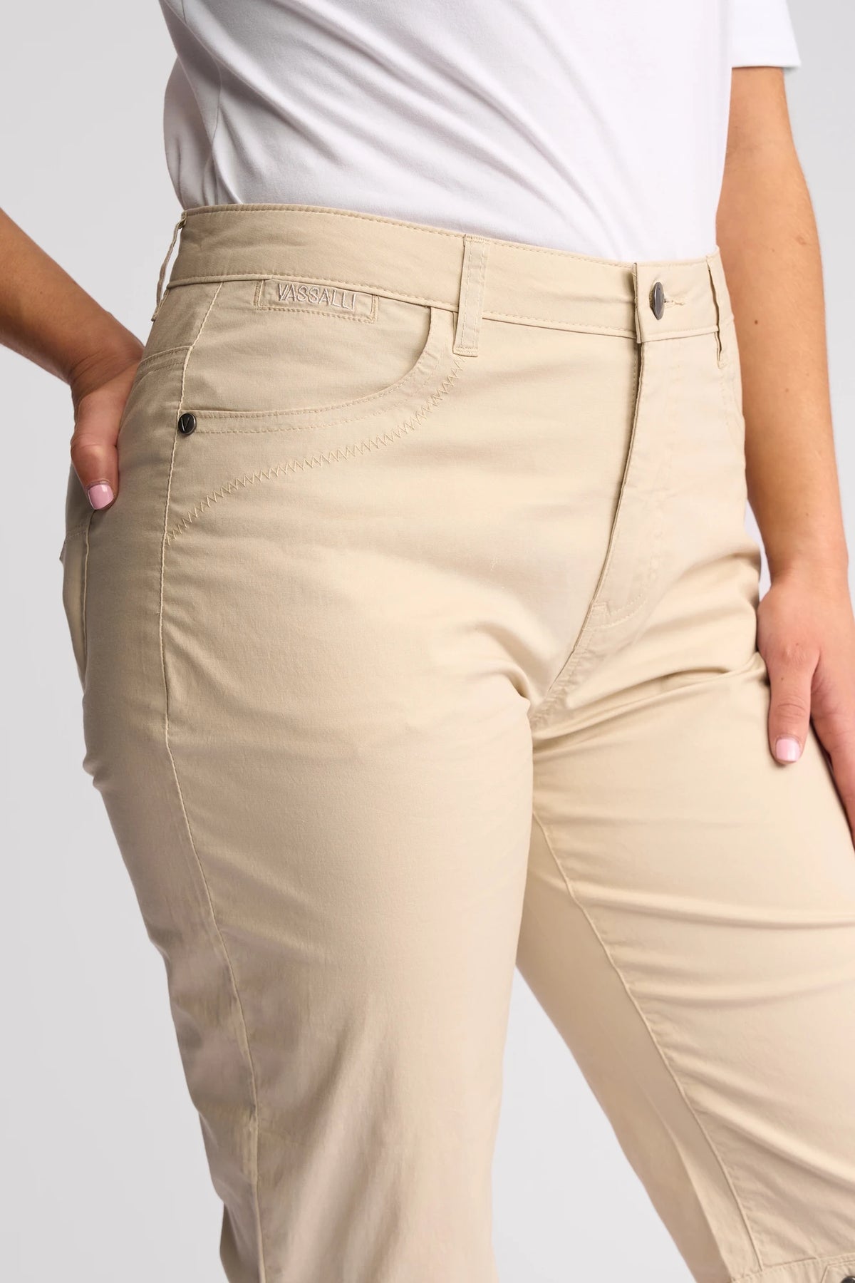 A person is wearing the Vassalli Custom Poplin Short in Sand, paired with a white shirt and posing with one hand on their hip. The photo focuses on the waist and upper legs, highlighting the details and fit of these summer staple shorts.