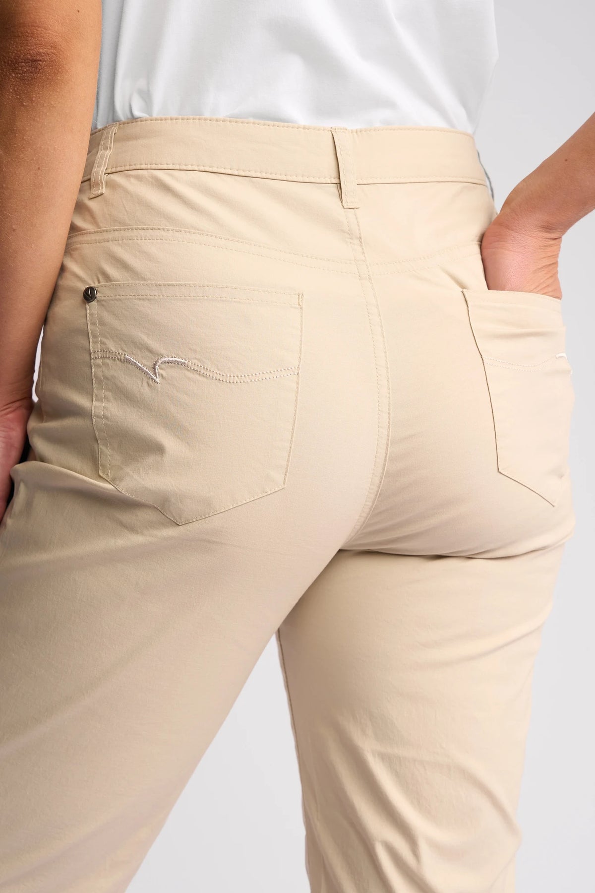 A person, photographed from behind with one hand in a back pocket, is wearing Vassalli’s Custom Poplin Short in Sand—a beige straight-leg short made from lightweight fabric. This summer staple features two back pockets with subtle stitching and is paired with a white shirt.